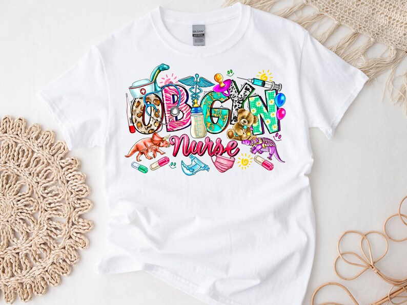 May include: White t-shirt with a colorful graphic design that says "OBGYN Nurse" with various medical and baby-related icons.