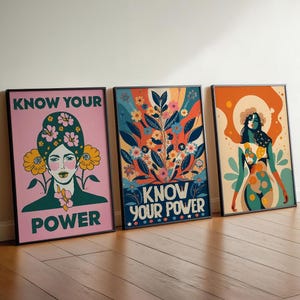 Könnte beinhalten: Drei gerahmte Kunstdrucke mit schwarzen Rändern. Die Drucke zeigen farbenfrohe Illustrationen von Frauen und floralen Designs. Der Text "KNOW YOUR POWER" ist auf zwei der Drucke zu sehen. Die Drucke lehnen an einem Holzboden.