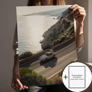 May include: A print depicting a classic silver car on a coastal road, with the sea and cliffs in the background. The image is taken on a sunny day. The print includes a black frame option.