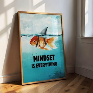 Può includere: Stampa artistica incorniciata con un pesce rosso con una pinna di squalo, che nuota in acqua blu. Il testo "MINDSET IS EVERYTHING" è visualizzato in grassetto, in lettere nere. L'opera d'arte è in una cornice di legno.