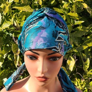 May include: A blue and purple patterned turban style head covering with a knot on top. The fabric has a soft, flowing look.
