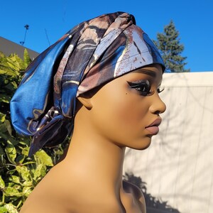 May include: A blue and brown patterned satin head wrap with gold accents. The wrap is tied in a turban style.