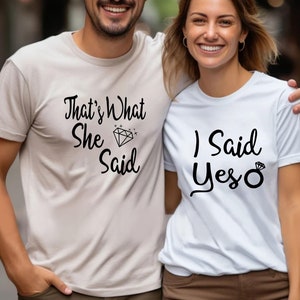 May include: A couple wearing matching engagement announcement t-shirts. The man's shirt says "That's What She Said" with a diamond graphic. The woman's shirt says "I Said Yes" with a ring graphic.