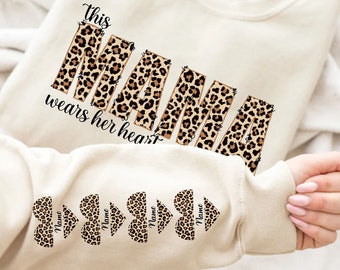 May include: A beige sweatshirt with the words "this mama wears her heart" in brown text with a leopard print design. The sleeves have four leopard print hearts with the word "Name" in each heart.