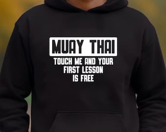 Könnte beinhalten: Schwarzer Kapuzenpullover mit dem Text "Muay Thai" in einem weißen Rechteck und dem Text "Touch me and your first lesson is free" in weiß unter dem Rechteck.