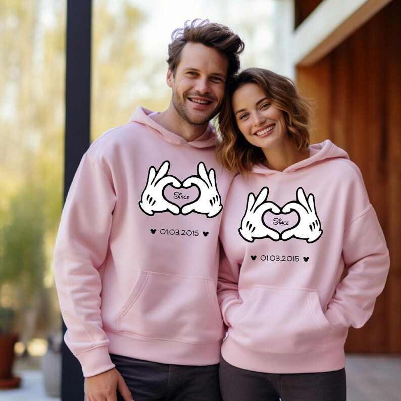 May include: Matching light pink hoodies with a heart-shaped hand design and the word "Since" inside the heart. The date "01.03.2015" is printed below the design. The hoodies have a front pocket and a hood.