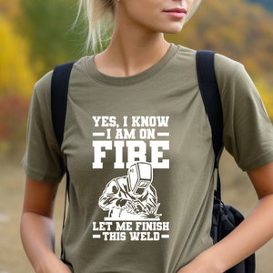 May include: A green t-shirt with a white graphic of a welder with the text "YES, I KNOW - I AM ON FIRE - LET ME FINISH - THIS WELD - "