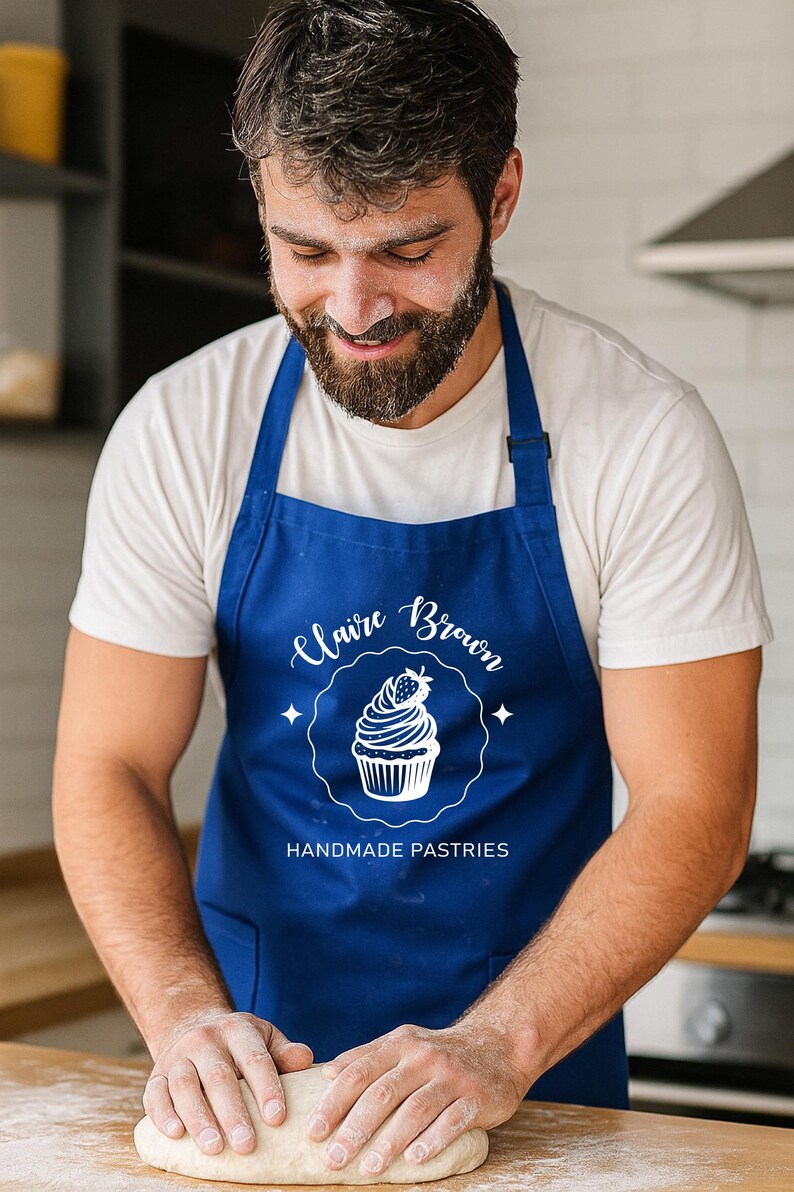 May include: A baker wearing a blue apron with the text "Claire Brown Handmade Pastries" and a cupcake design. The baker is working with dough on a wooden surface, with flour dusted on the surface and the baker's face.