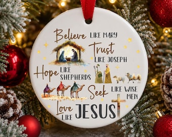 May include: A round white ceramic Christmas ornament hanging from a red ribbon. It features a nativity scene illustration and text that reads: Believe like Mary, Trust like Joseph, Hope like Shepherds, Seek like Wise Men, Love like Jesus, with a cross.
