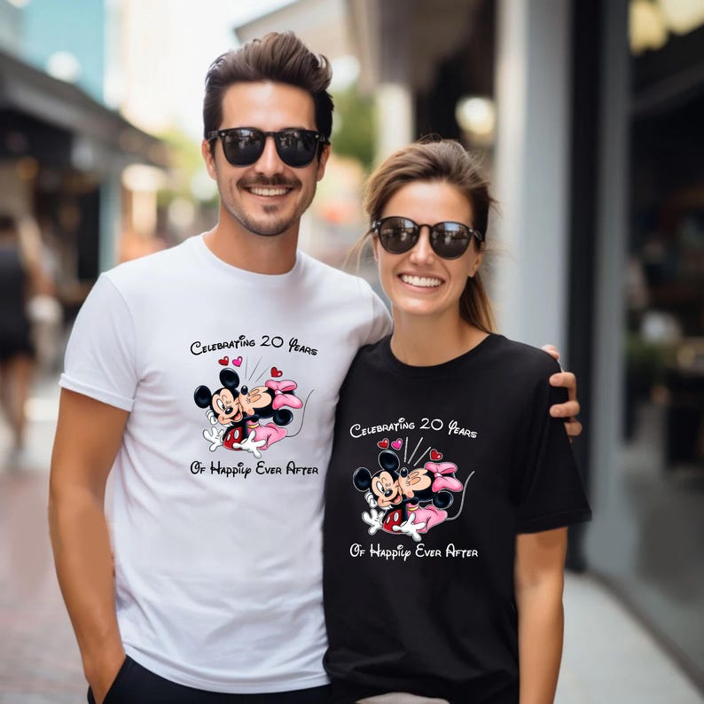 May include: A white t-shirt and a black t-shirt featuring a cartoon image of Mickey and Minnie Mouse embracing, with the text "Celebrating 20 Years Or Happily Ever After". The shirts are worn by a couple.
