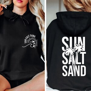 May include: Black hooded sweatshirt with the text "SUN SALT SAND" and a palm tree graphic on the front and back.