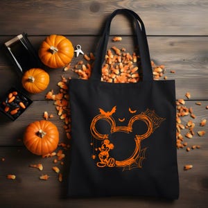 Puede incluir: Una bolsa de tela negra con un gr&aacute;fico naranja de una silueta de Mickey Mouse delineada en estilo garabateado. El dise&ntilde;o incluye peque&ntilde;os murci&eacute;lagos, telara&ntilde;as y una peque&ntilde;a figura de Mickey Mouse de pie en la base del contorno circular.