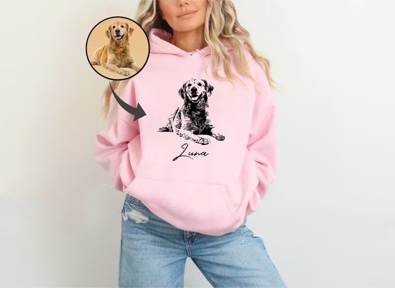 May include: A pink hoodie with a black and white illustration of a dog on the front. The dog is lying down and the text "Luna" is written below it.