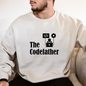 May include: A white sweatshirt with a black graphic design that says "The CodeFather" with a person sitting at a laptop with code symbols and a gear above them.