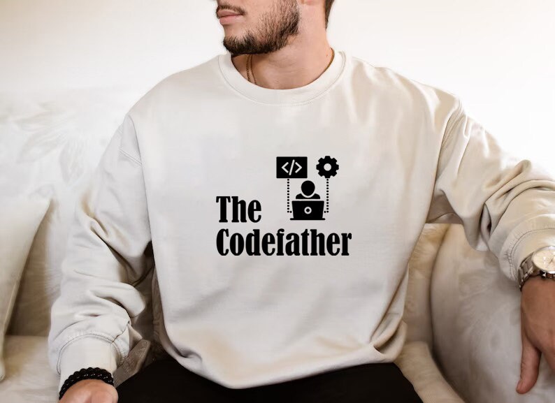 May include: A white sweatshirt with a black graphic design that says "The CodeFather" with a person sitting at a laptop with code symbols and a gear above them.