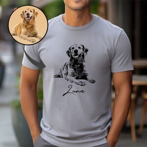 May include: A grey t-shirt featuring a black and white illustration of a dog lying down. The dog's name, "Luna", is written in cursive below the illustration.