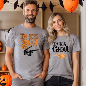 May include: Two gray t-shirts with Halloween-themed graphics. One shirt says "I'm Her Boo" with an orange and black skeleton hand pointing. The other says "I'm His Ghoul" with an orange skeleton hand pointing.