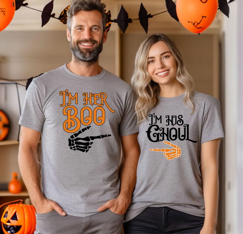 May include: Two gray t-shirts with Halloween-themed graphics. One shirt says "I'm Her Boo" with an orange and black skeleton hand pointing. The other says "I'm His Ghoul" with an orange skeleton hand pointing.