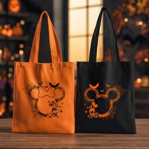 Puede incluir: Dos bolsas de tela, una naranja y otra negra, cada una con un gr&aacute;fico de una silueta de orejas de rat&oacute;n con telara&ntilde;as y murci&eacute;lagos. La bolsa naranja muestra un estampado negro, mientras que la bolsa negra tiene un estampado naranja.