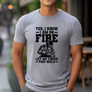 May include: Gray t-shirt with a black graphic of a welder and the text "Yes, I know I am on fire. Let me finish this weld."