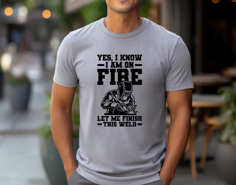 May include: Gray t-shirt with a black graphic of a welder and the text "Yes, I know I am on fire. Let me finish this weld."