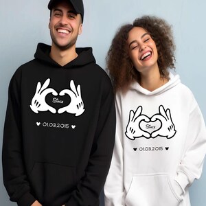 May include: Black and white matching hoodies. The black hoodie has a white graphic of cartoon hands forming a heart, with the word "Since" inside the heart and the date "01.03.2015" below. The white hoodie has the same design.