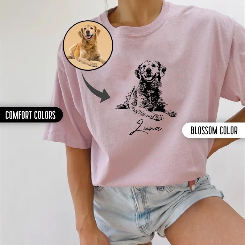 K&ouml;nnte beinhalten: Ein pinkfarbenes T-Shirt mit einer schwarz-wei&szlig;en Illustration eines Hundes. Der Hund liegt und der Text "Luna" steht darunter. Das Shirt wird von einem Model getragen, das eine Jeans-Shorts tr&auml;gt.