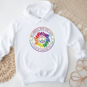 Pu&ograve; includere: Felpa con cappuccio bianca con un simbolo di pace arcobaleno e il testo "Fai attenzione a chi odi, potrebbe essere qualcuno che ami."