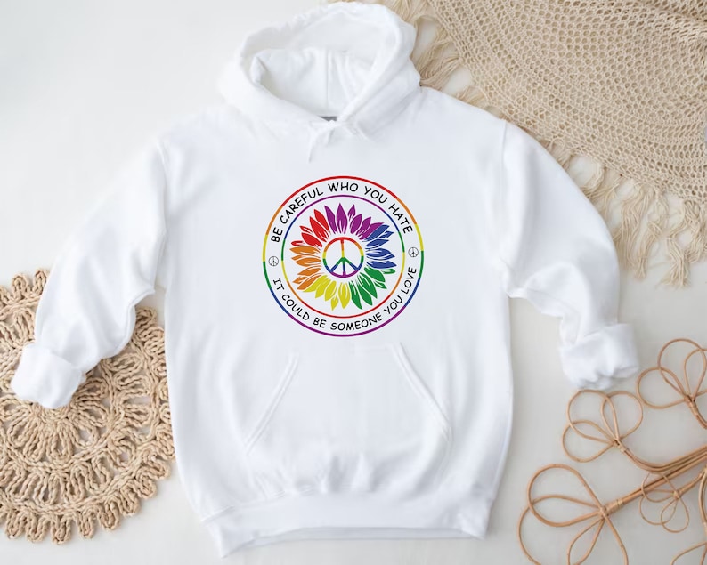 Pu&ograve; includere: Felpa con cappuccio bianca con un simbolo di pace arcobaleno e il testo "Fai attenzione a chi odi, potrebbe essere qualcuno che ami."
