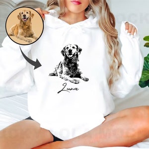 May include: White hoodie with a black and white illustration of a golden retriever dog. The dog is lying down and the text "Luna" is written below the dog.