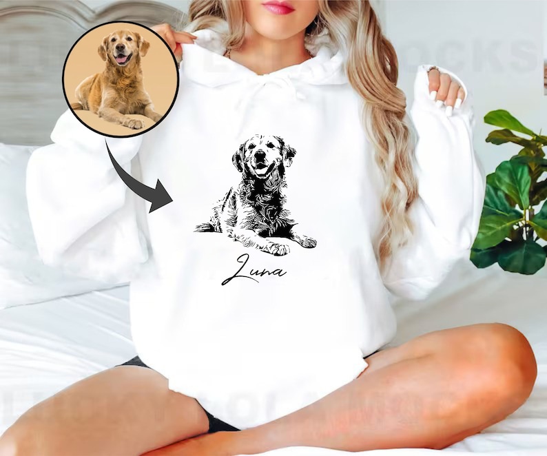 May include: White hoodie with a black and white illustration of a golden retriever dog. The dog is lying down and the text "Luna" is written below the dog.
