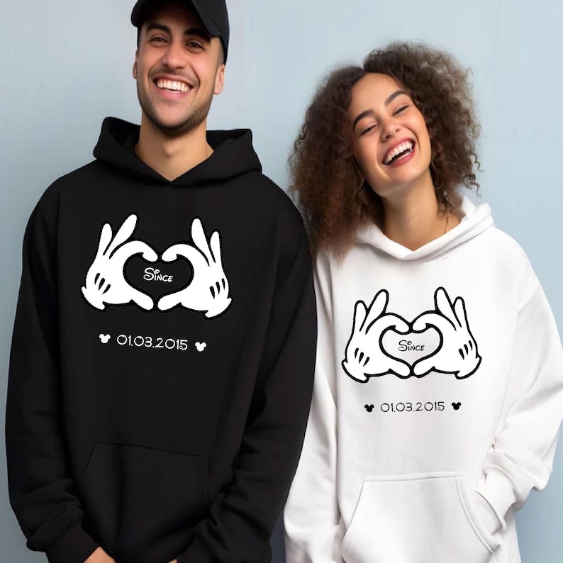 May include: Black and white matching hoodies. The black hoodie has a white graphic of gloved hands forming a heart, with the word "Since" inside the heart and the date "01.03.2015" below. The white hoodie has the same design.