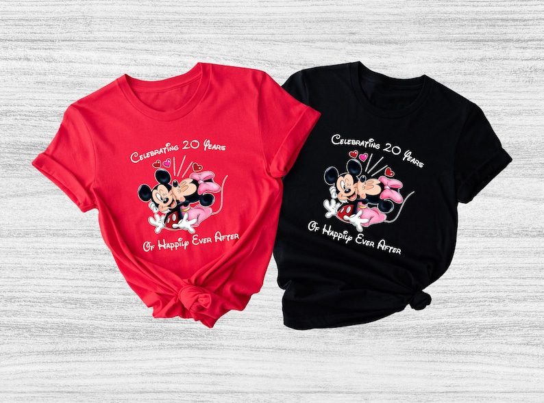 May include: Two t-shirts, one red and one black, featuring a graphic of Mickey and Minnie Mouse kissing. The text on the shirts reads "Celebrating 20 Years Of Happily Ever After."