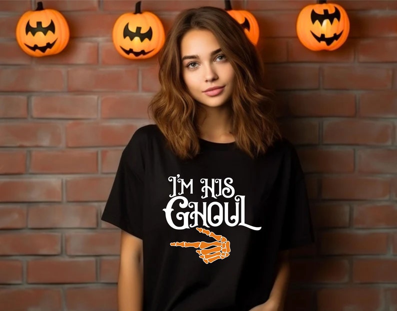 May include: Black t-shirt with the text "I'M HIS GHOUL" in white, and an orange skeleton hand pointing to the right. The shirt is a Halloween-themed design.
