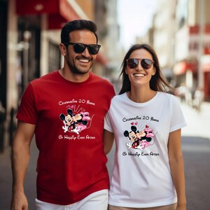 May include: A couple wearing matching t-shirts. The red shirt features Mickey and Minnie Mouse with the text "Celebrating 20 Years Of Happily Ever After." The white shirt has the same design. Both shirts have a crew neck and short sleeves.