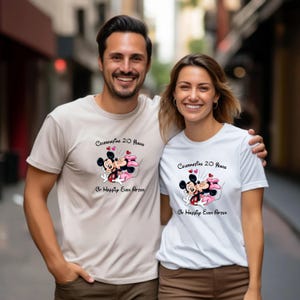 May include: Two people wearing matching t-shirts. The shirts are beige and white, each featuring a graphic of Mickey and Minnie Mouse embracing, with hearts and the text "Celebrating 20 Years Or Happily Ever After."