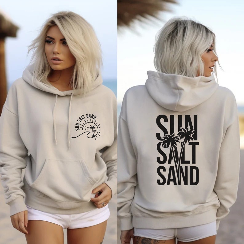 May include: A light beige hoodie with a black graphic on the front that says "Sun Salt Sand" with a sun, wave, and palm trees. The back of the hoodie has a black graphic that says "Sun Salt Sand" with palm trees.