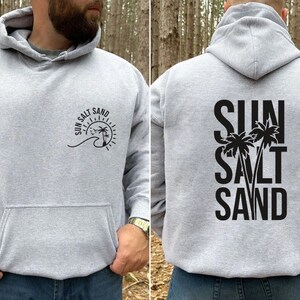 May include: A gray hooded sweatshirt with a black graphic on the front that says "Sun Salt Sand" with a palm tree and wave design. The back of the sweatshirt has a black graphic that says "Sun Salt Sand" with two palm trees.