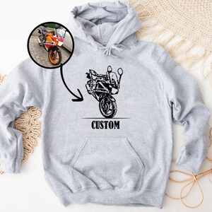 May include: Gray hooded sweatshirt with a black and white illustration of a motorcycle on the front. The text "CUSTOM" is printed below the motorcycle.