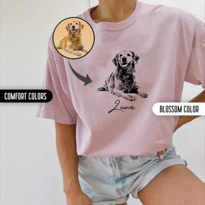 K&ouml;nnte beinhalten: Ein pinkfarbenes T-Shirt mit einer schwarz-wei&szlig;en Illustration eines Hundes. Der Hund liegt und der Text "Luna" steht darunter. Das Shirt wird von einem Model getragen, das eine Jeans-Shorts tr&auml;gt.