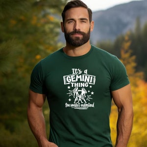 May include: A dark green t-shirt with the text "It's a GEMINI THING you wouldn't understand" in white. The graphic includes the Gemini zodiac symbol. The shirt is being worn by a person.