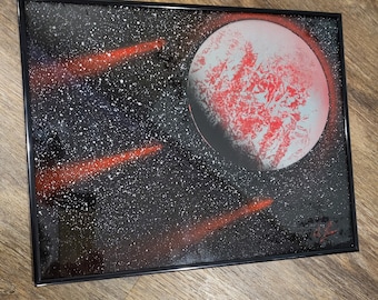 May include: A black framed canvas painting of a red planet with white craters against a black background with white stars and red streaks of light.