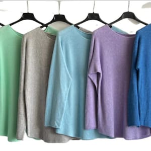 May include: A collection of long-sleeved tops in a spectrum of colours: olive green, white, cerise, mint, grey, light blue, lilac, blue, pink, and beige. Each top is displayed on a black hanger against a white backdrop.