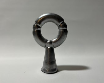 Könnte beinhalten: Ein silberner Vorhang-Abschluss aus Metall mit einem Ring oben und einer spitzen Basis.