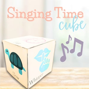 May include: A white cube with different activities printed on each side. The activities include "Slow", "Whisper", and a musical note. The cube is labeled "Singing Time Cube".