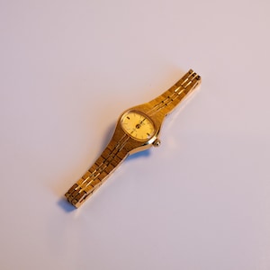 May include: A gold-tone wristwatch with a round face and a gold-tone metal band.