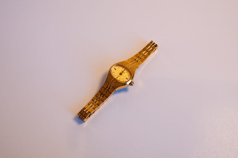 May include: A gold-tone wristwatch with a round face and a gold-tone metal band.