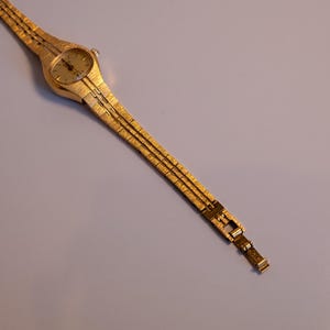 May include: A gold-toned wristwatch with a round face and a gold-toned metal band.