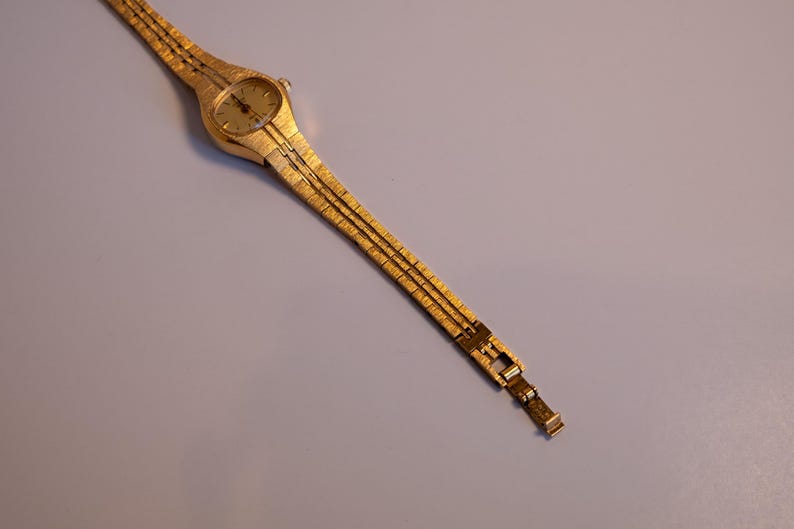 May include: A gold-toned wristwatch with a round face and a gold-toned metal band.