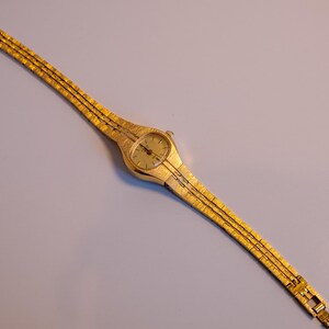 May include: A gold-toned wristwatch with a round face and a gold metal band.